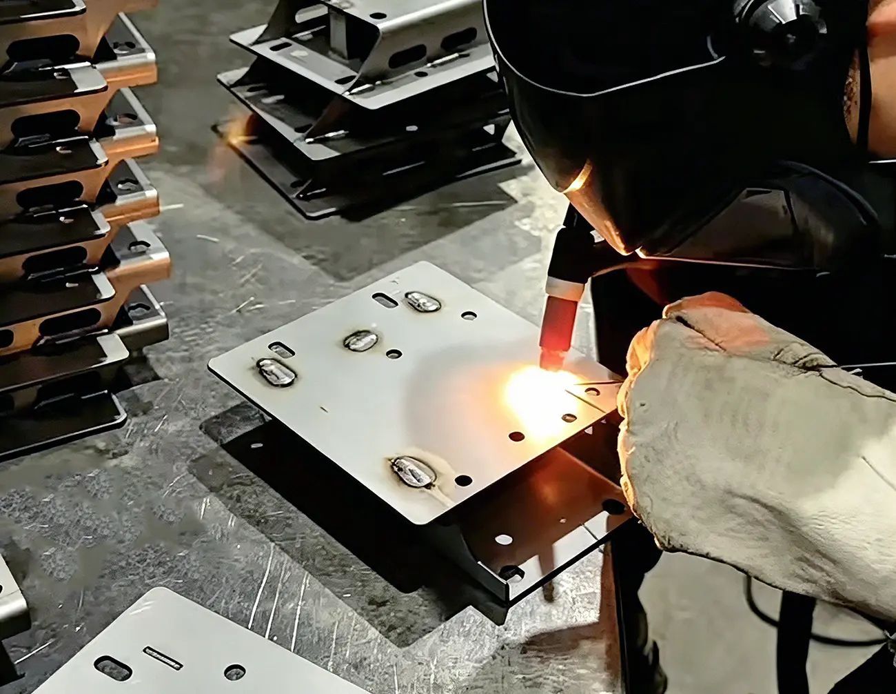 Skilled welder carrying out TIG welding on stainless steel sheet metal bracket inside fabrication workshop