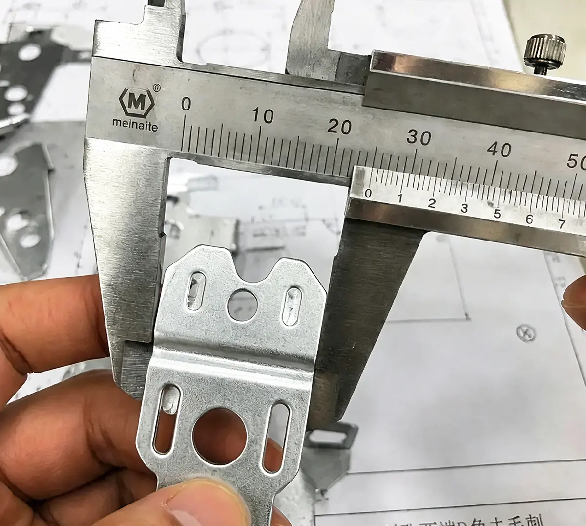 Inspector measuring a stamped sheet-metal bracket with a vernier caliper