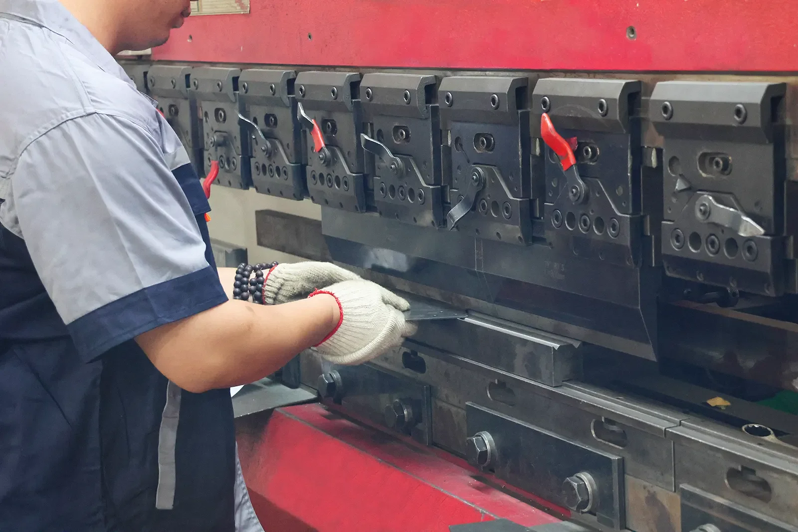 Worker operating CNC press brake to bend steel sheet for custom EV charger enclosure fabrication
