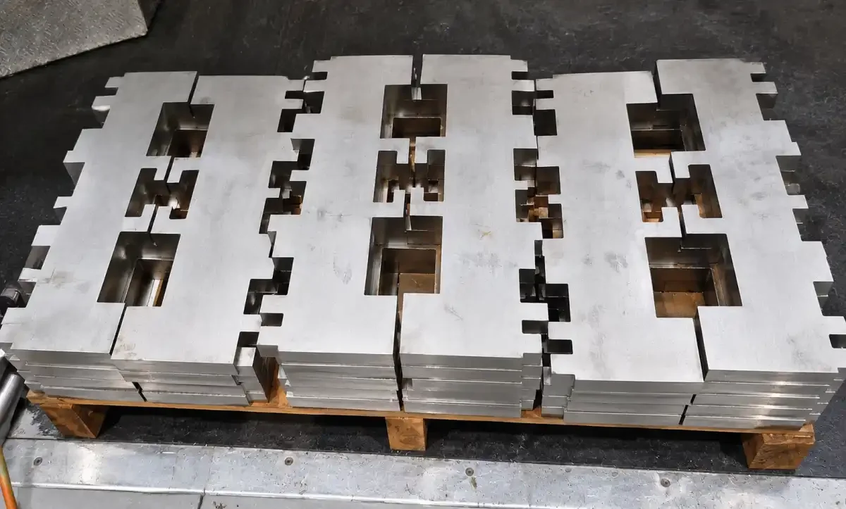 Stacks of laser-cut stainless steel blanks prepared for manifold fabrication.